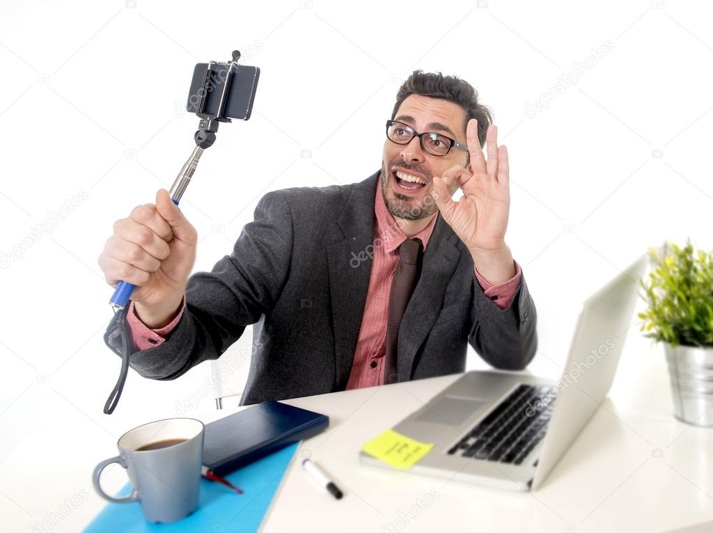 funny nerd businessman at office desk taking selfie photo with mobile phone camera and stick