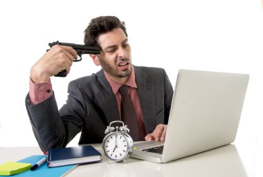 businessman at office desk working on computer laptop pointing gun on his tempo in suicide gesture
