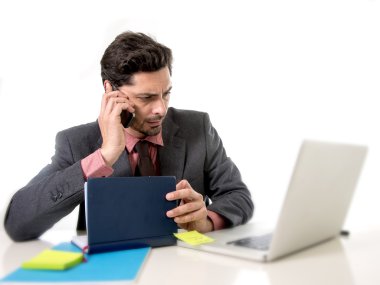 attractive businessman sitting at office desk working in stress on computer laptop talking on mobile phone overworked