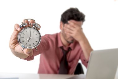 depressed businessman holding alarm clock sitting at office desk working with computer laptop in deadline project concept