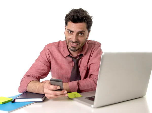 Hombre de negocios que trabaja en el escritorio de la oficina mensajes de texto con el teléfono móvil delante de la computadora portátil sonriendo feliz — Foto de Stock