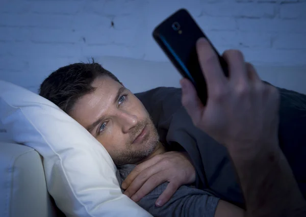 Young man in bed couch at home late at night using mobile phone in low light relaxed in communication technology concept — Stock fotografie