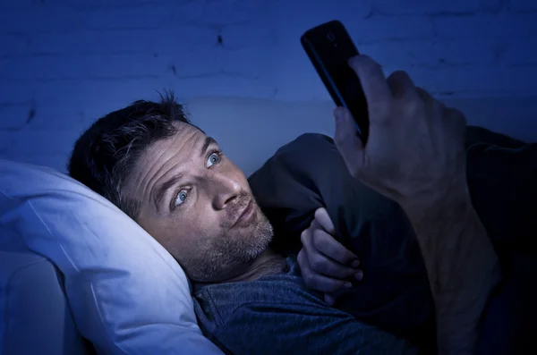 Hombre en la cama sofá en casa tarde en la noche utilizando el teléfono móvil en baja —  Fotos de Stock
