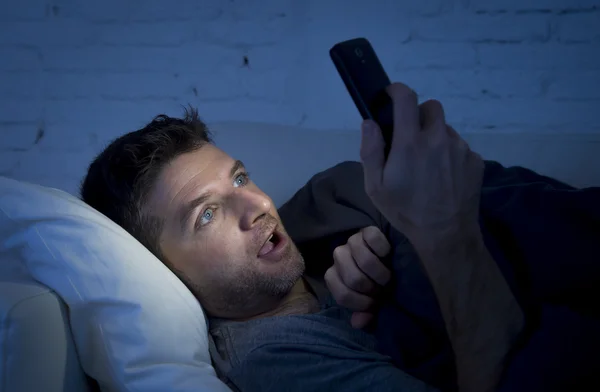 Hombre en la cama sofá en casa tarde en la noche usando el teléfono móvil en la luz baja viendo porno en línea —  Fotos de Stock