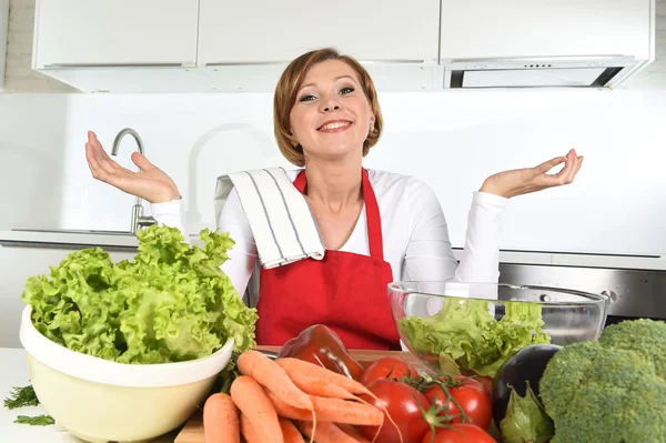 Young beautiful woman in red apron at home kitchen preparing vegetable salad bowl smiling happy — Stock fotografie