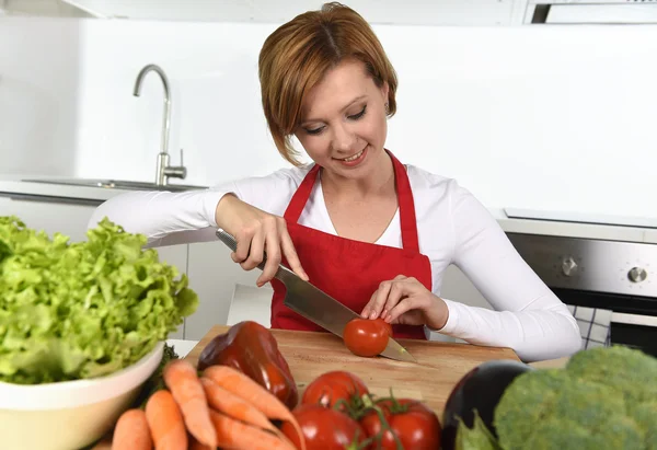 Happy woman at home kitchen preparing vegetable salad with lettuce carrots and slicing tomato — Stock Photo, Image