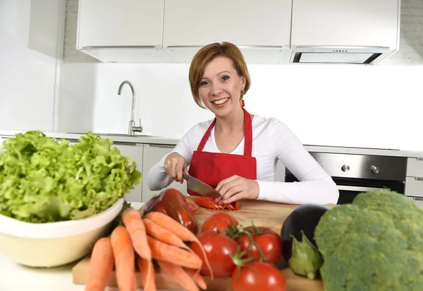 Happy woman at home kitchen preparing vegetable salad with lettuce carrots and slicing tomato — ストック写真