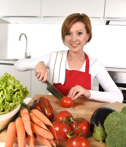 Happy woman at home kitchen preparing vegetable salad with lettuce carrots and slicing tomato — Zdjęcie stockowe