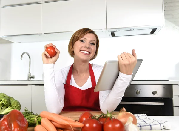 Happy home cook woman in apron at  kitchen using digital tablet as cookbook — Stockfoto