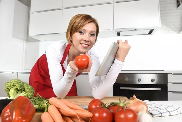 Casa feliz cozinheiro mulher no avental na cozinha usando tablet digital como livro de receitas — Fotografia de Stock