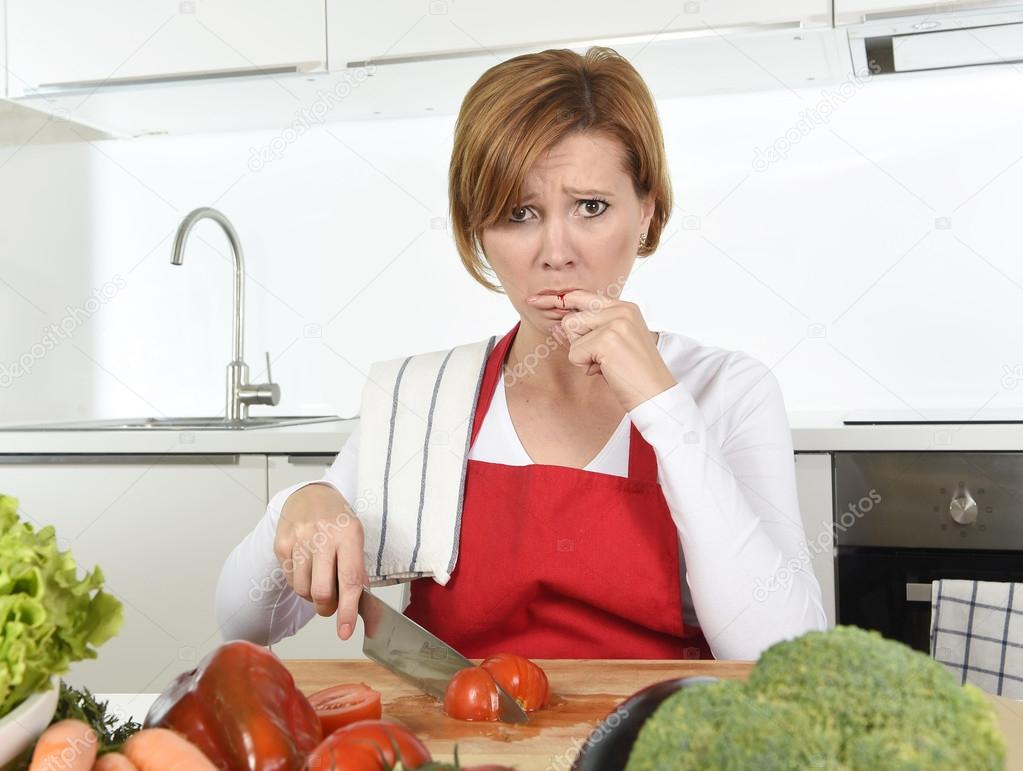 home cook woman in red apron slicing carrot with kitchen knife suffering domestic accident cutting hurting finger