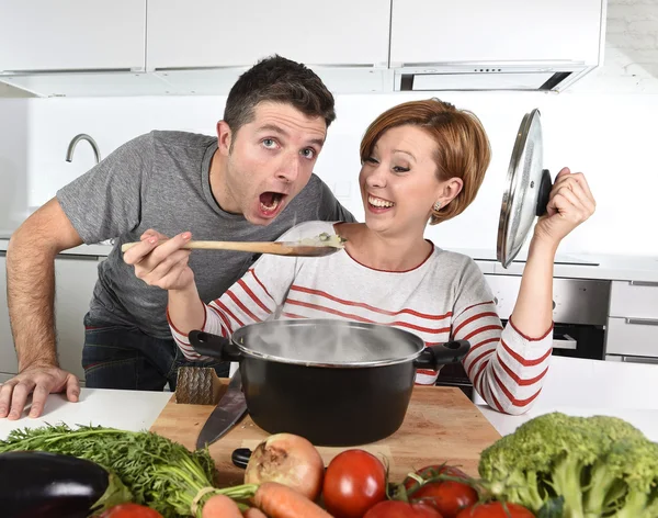Junges attraktives Paar zu Hause Küche mit Mann Verkostung Gemüseeintopf von ihrer Frau glücklich lächelnd gekocht — Stockfoto