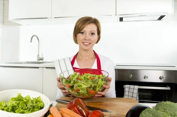 Молодая красивая домохозяйка на современной кухне готовит овощной салат миску улыбаясь счастливой — стоковое фото