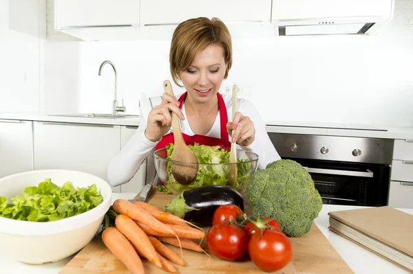 Молодая красивая домохозяйка на современной кухне готовит овощной салат миску улыбаясь счастливой — стоковое фото