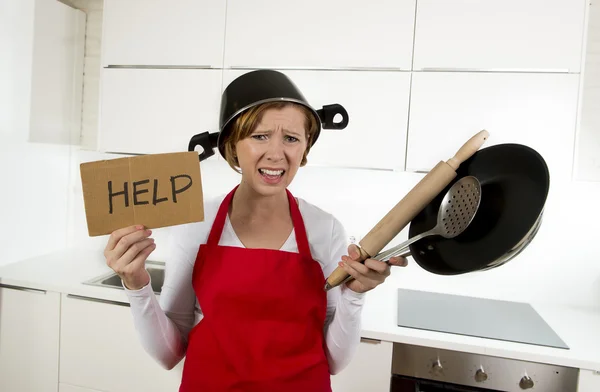 Junge attraktive Hausfrau in roter Schürze in der Küche hält Pfanne und Haushalt mit Topf auf dem Kopf im Stress — Stockfoto