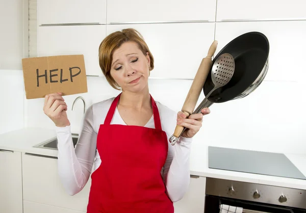 Home cook woman in red apron at domestic kitchen holding pan and household in stress — Stock Photo, Image