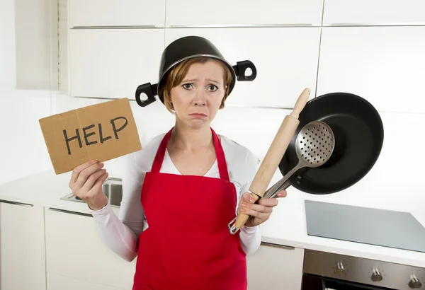 Junge attraktive Hausfrau in roter Schürze in der Küche hält Pfanne und Haushalt mit Topf auf dem Kopf im Stress — Stockfoto