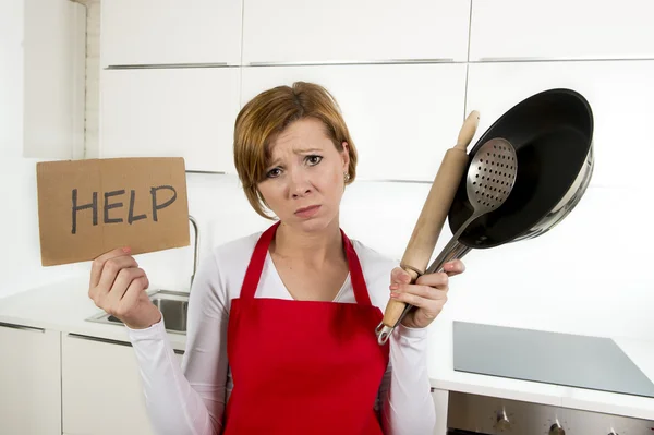 Home cook woman in red apron at domestic kitchen holding pan and household in stress — Stock Photo, Image