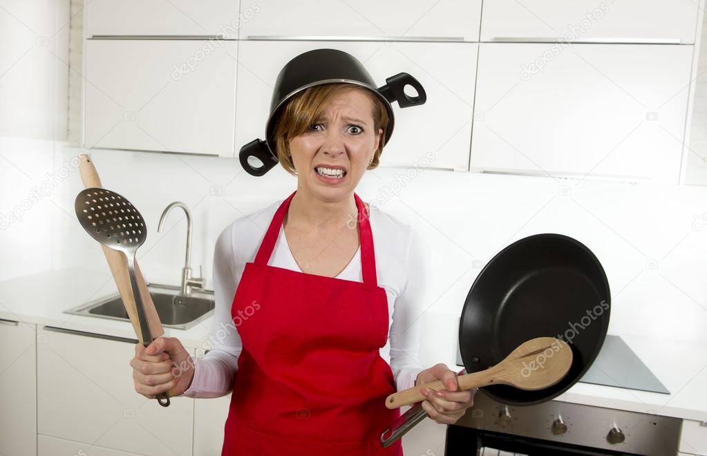 young attractive home cook woman in red apron at  kitchen holding pan and household with pot on her head in stress