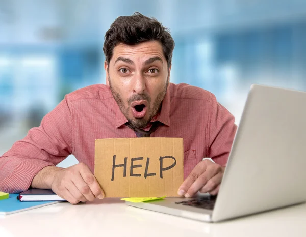 Hombre de negocios en el escritorio de la oficina trabajando en computadora portátil pidiendo ayuda sosteniendo cartel de cartón triste deprimido — Foto de Stock