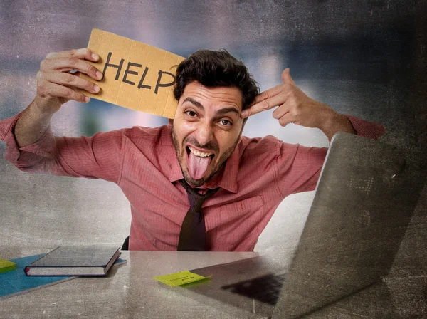 Бизнесмен в офисе работает на ноутбуке, прося о помощи, держа картонную табличку в депрессии — стоковое фото