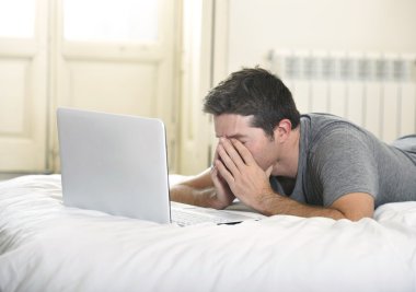 young tired man lying on bed or couch working on computer laptop at home wireless connected to internet in technology concept