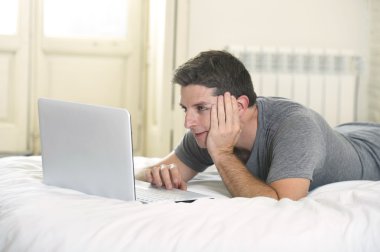 young attractive man lying on bed or couch enjoying social networking using computer laptop at home