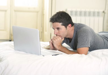 young attractive man lying on bed or couch enjoying social networking using  computer laptop at home