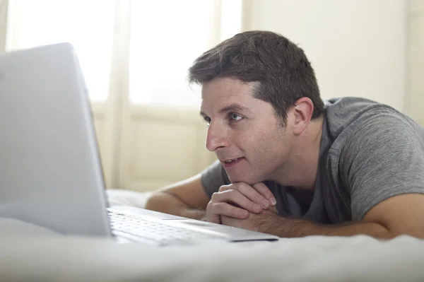Porträt eines jungen attraktiven Mannes, der auf dem Bett liegt und sich einen Online-Film im Computer-Laptop zu Hause im Internet-Konzept ansieht — Stockfoto