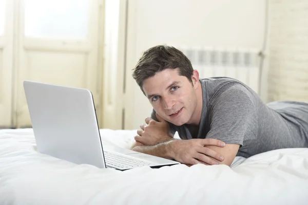 Junger attraktiver Mann liegt auf Bett oder Couch und genießt soziale Netzwerke mit Computer-Laptop zu Hause — Stockfoto
