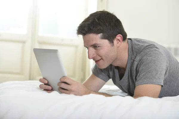 Jovem homem atraente deitado na cama ou no sofá desfrutando de redes sociais usando tablet digital internet computador em casa — Fotografia de Stock