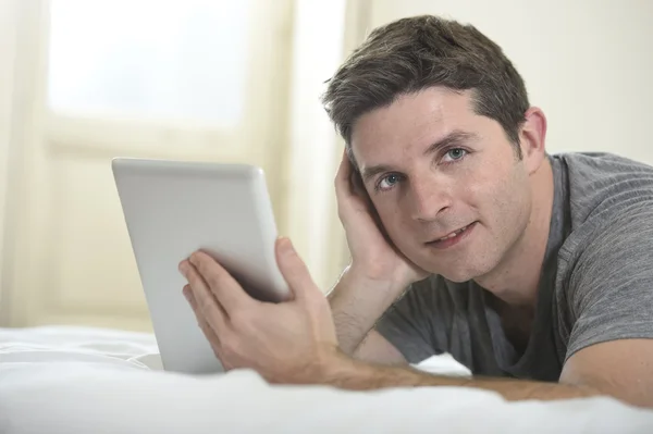 Jovem homem atraente deitado na cama ou no sofá desfrutando de redes sociais usando tablet digital internet computador em casa — Fotografia de Stock