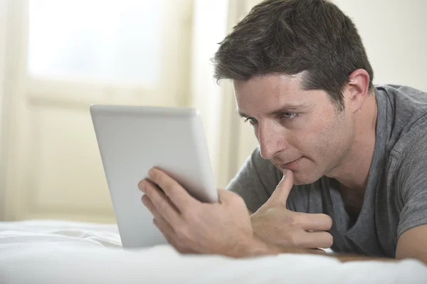 Joven atractivo hombre acostado en la cama o sofá disfrutando de las redes sociales utilizando tableta digital de Internet en casa —  Fotos de Stock