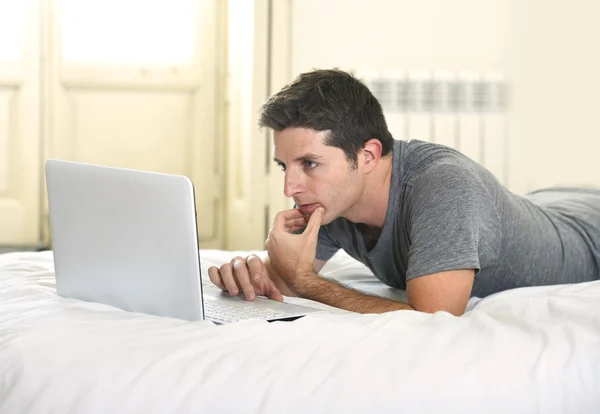 Молодой привлекательный мужчина лежит на кровати или диване, работая на компьютере ноутбука типирования подключен к Интернету — стоковое фото