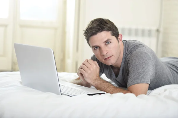 Young attractive man lying on bed or couch enjoying social networking using  computer laptop at home wireless internet — Stockfoto