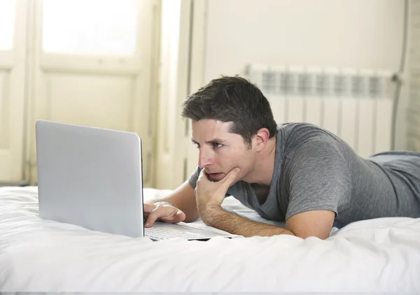 Young attractive man lying on bed or couch enjoying social networking using  computer laptop at home wireless internet — Stok fotoğraf