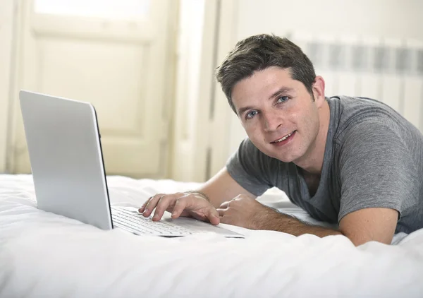 Young attractive man lying on bed or couch enjoying social networking using computer laptop at home — Stock fotografie