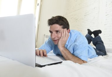young attractive man lying on bed enjoying social networking using laptop at home