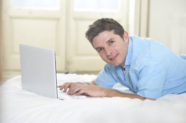 young attractive man lying on bed enjoying social networking using computer at home