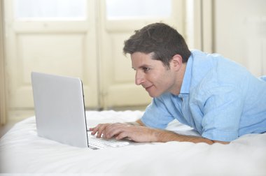 young attractive man lying on bed enjoying social networking using laptop at home