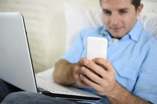 Close up hands of man lying on bed couch using mobile phone and computer working from home — ストック写真