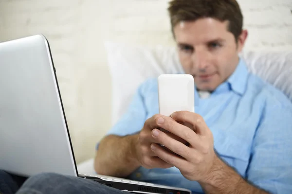 Cerrar las manos del hombre acostado en el sofá de la cama usando el teléfono móvil y la computadora que trabaja desde casa —  Fotos de Stock