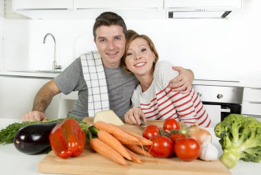 young American couple working at home kitchen preparing vegetable salad together smiling happy