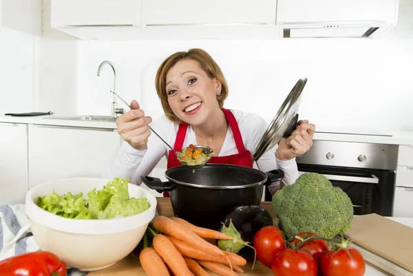 Giovane casa felice cuoca donna in grembiule rosso in cucina domestica in possesso di pentola degustazione zuppa calda — Foto Stock