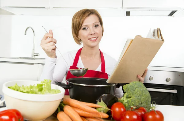 Mulher cozinheira atraente preparando sopa de guisado vegetal leitura receita livro de receitas na cozinha doméstica — Fotografia de Stock