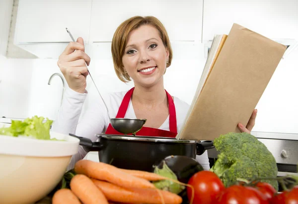 Atractiva mujer cocinera preparando sopa de estofado de verduras lectura receta libro de cocina en la cocina doméstica — Foto de Stock