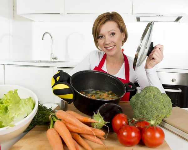 Cocinera casera mujer en delantal rojo en la cocina doméstica sosteniendo olla de cocina con sopa caliente olor a estofado de verduras —  Fotos de Stock