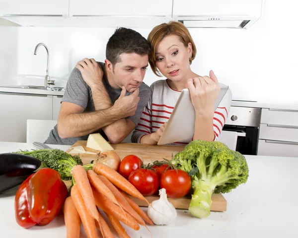 Pareja americana en la cocina doméstica esposa siguiendo la receta en almohadilla digital trabajando junto con el marido — Foto de Stock