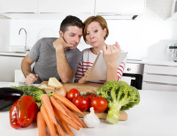 American couple in domestic kitchen wife following recipe in digital pad working together with husband — Stock Photo, Image