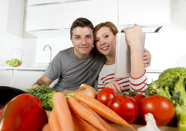 Pareja americana en la cocina doméstica esposa siguiendo la receta en almohadilla digital trabajando junto con el marido — Foto de Stock